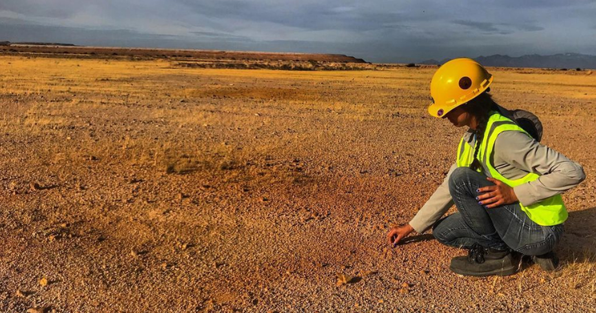 woman in hard-hat kneeling and touching the soil