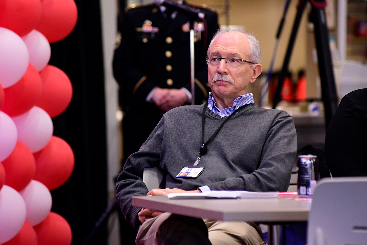 Rick Woychik sitting at a table with red and white balloons to his left