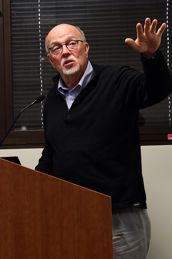 William Suk, Ph.D. stands at podium with left arm raised