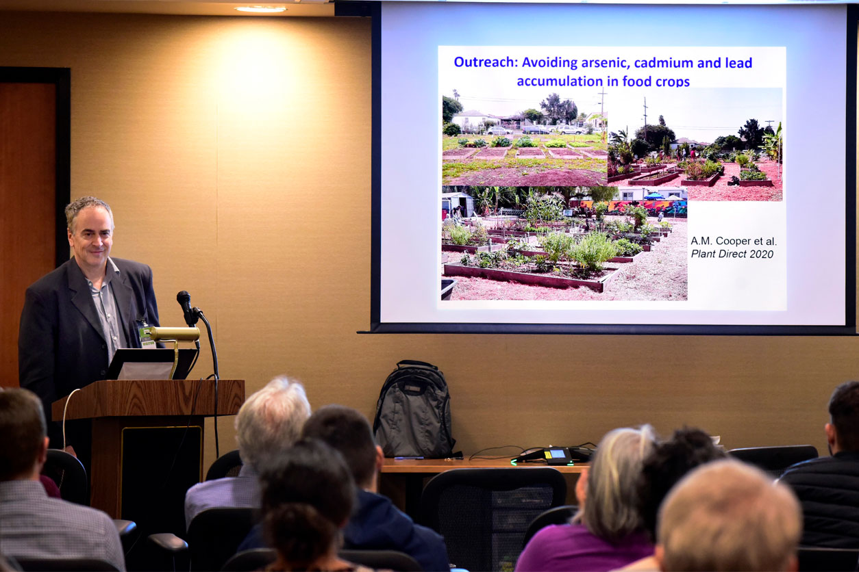 Julian Schroeder, Ph.D. stands near projector screen and speaks to the audience