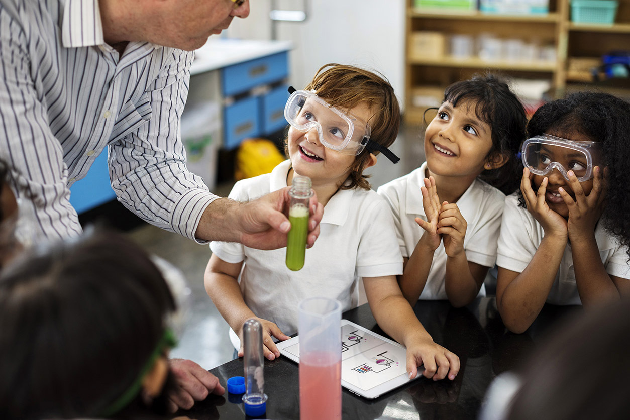students gathered around a table watching teacher demonstrate experiment with test tubes