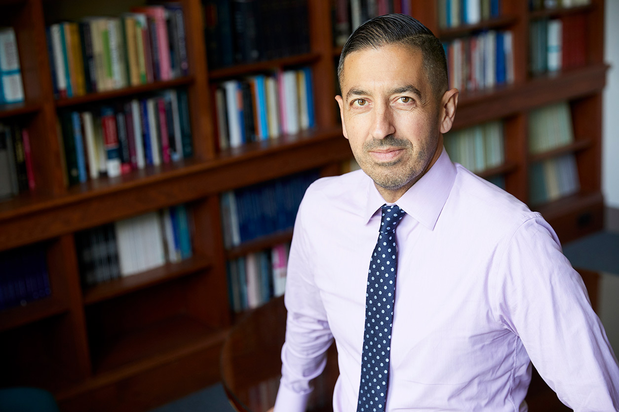Sandro Galea stands in front of bookshelves