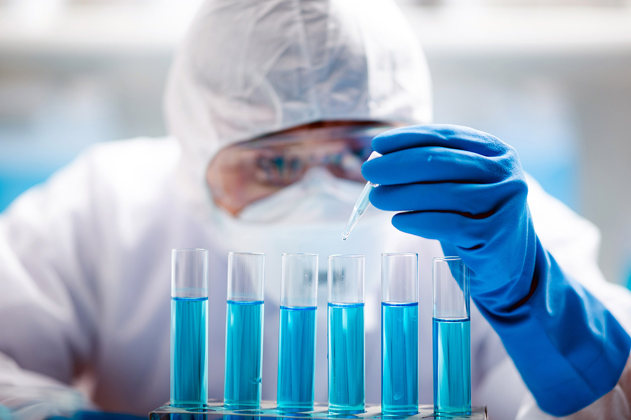 Scientist in protective gear filles six test tubes with blue liquid